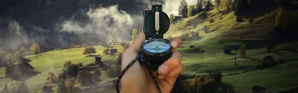 Image of a hand holding a compass on a foggy landscape.
