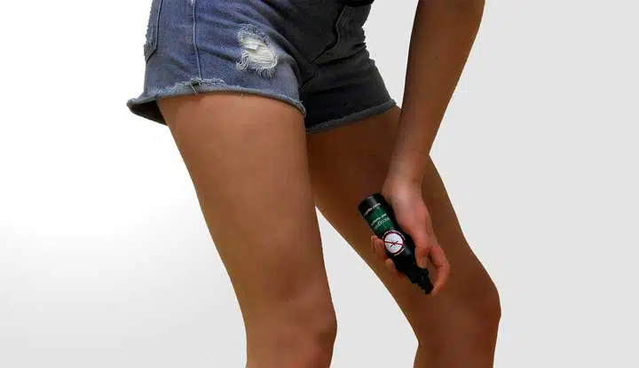 Photo of a girl spraying her legs with insect repellent. 