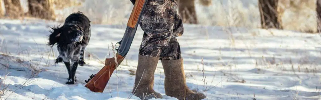 Photo of a hunter with cold weather hunting boots and a hunting dog.