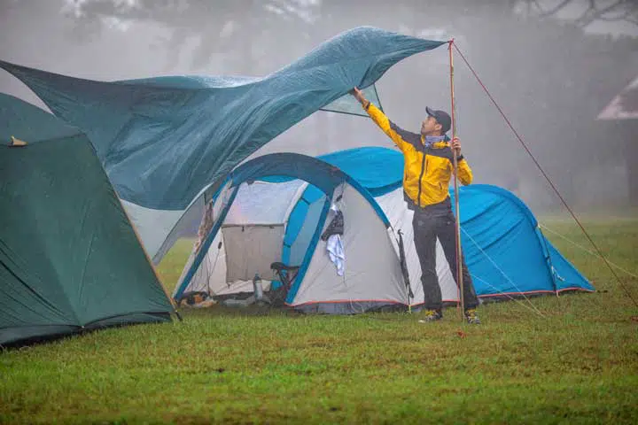 Photo of a guy protecting the tent under the rain. 