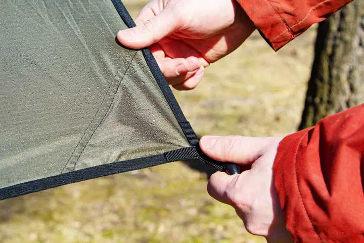Close-up of male hands and the corner of an tarp with a grommet. 