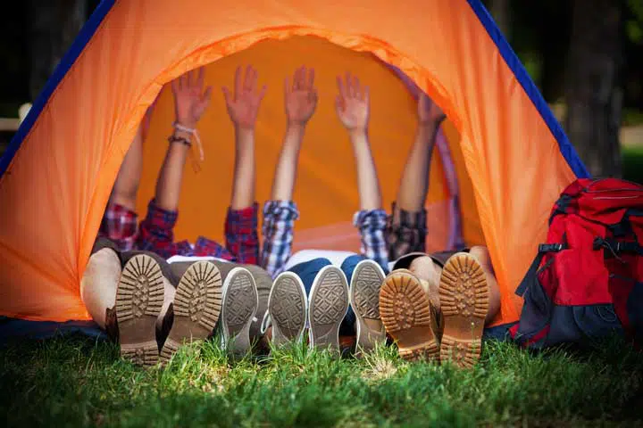 Group of young campres lying down in a tent with their hands up. 